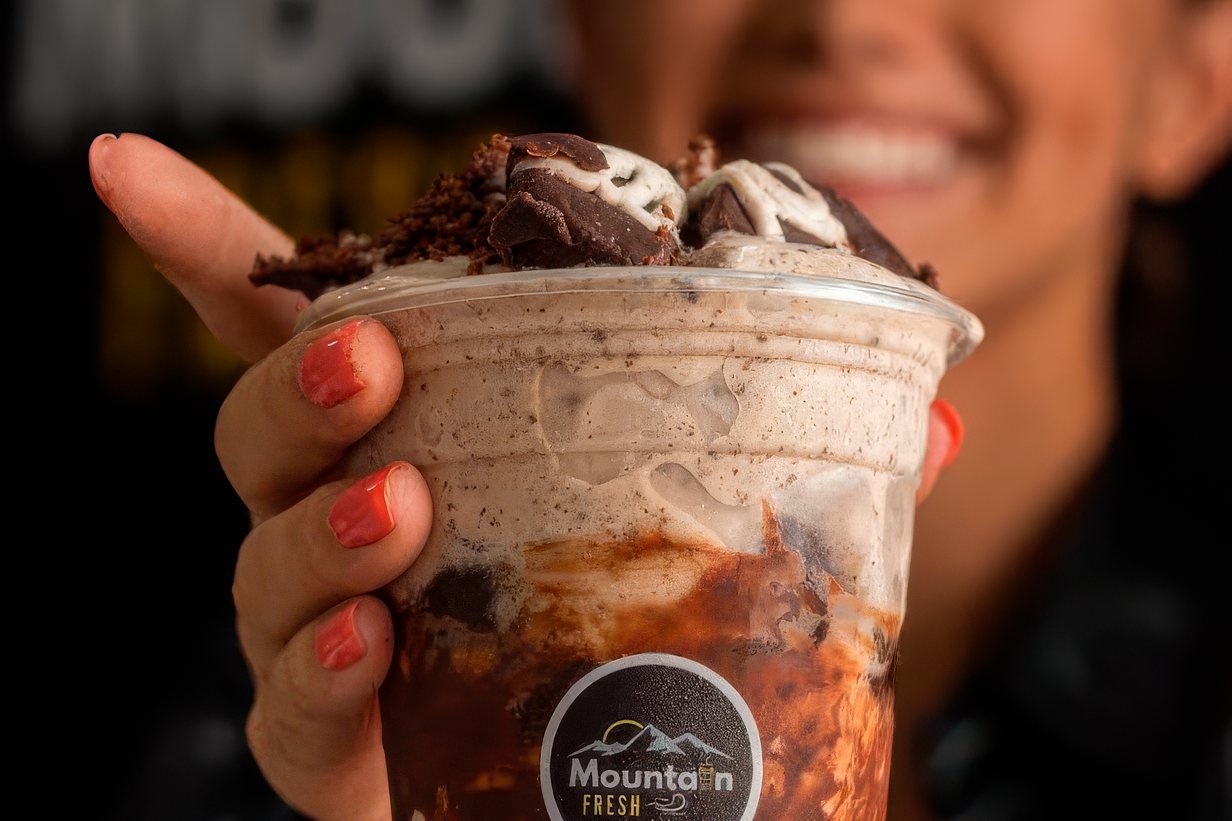 Un vaso de helado con sirope de chocolate ofrecido con las dos manos
